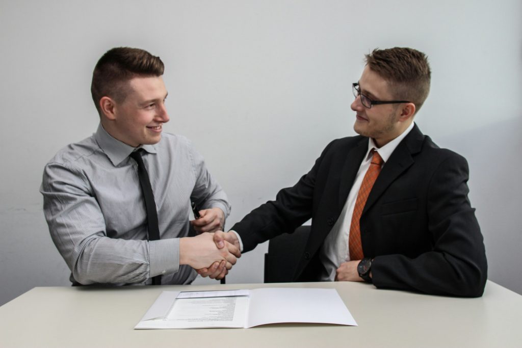 Two people sat at a desk shaking hands discussing ITSM and TBM
